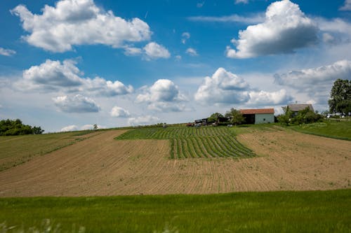 A field with a farm and some clouds in the sky