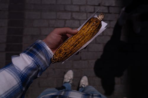 A person holding a corn on the cob in their hand