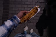 A person holding a corn on the cob in their hand