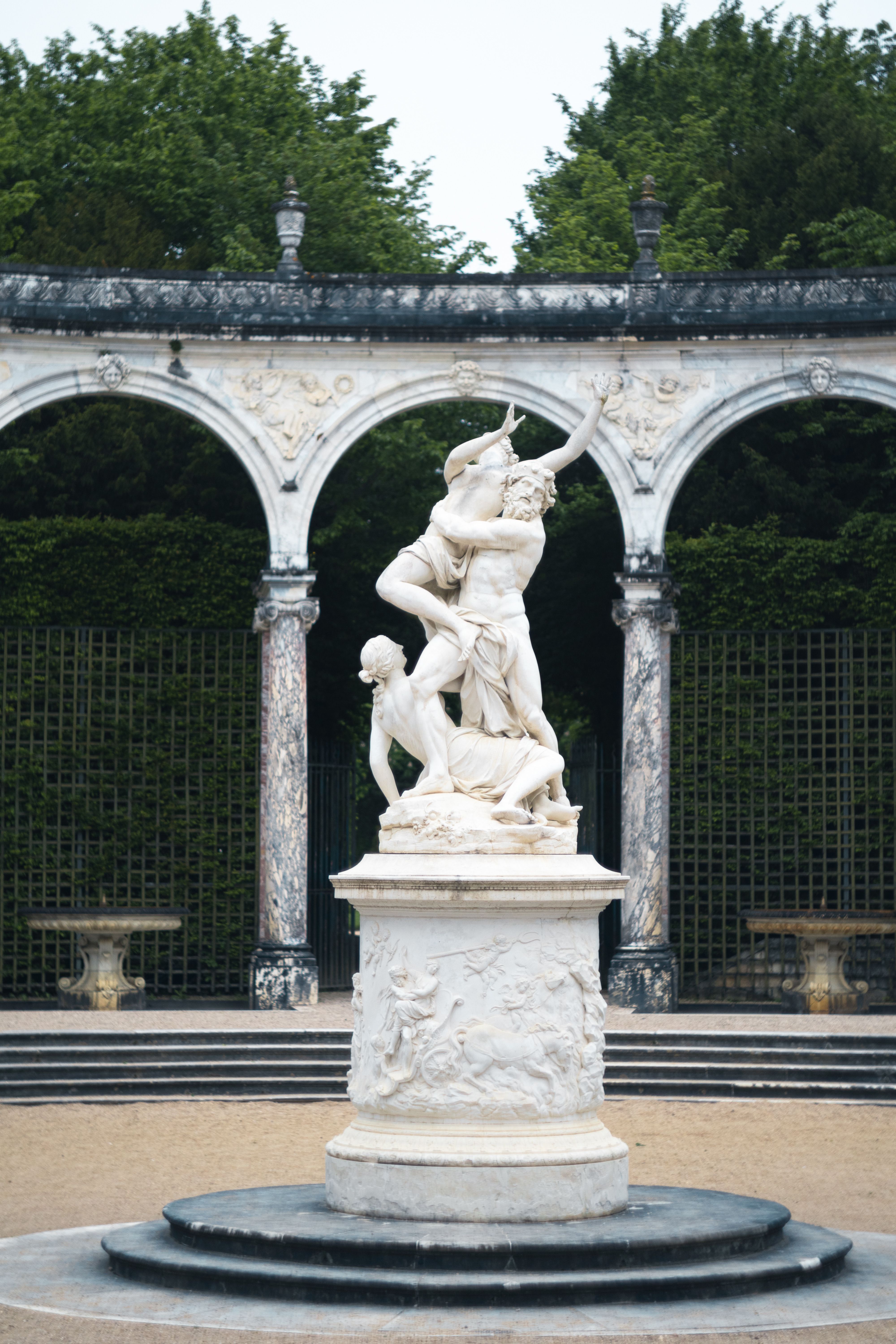 Elegant marble sculpture amidst classical arches in a lush garden setting.