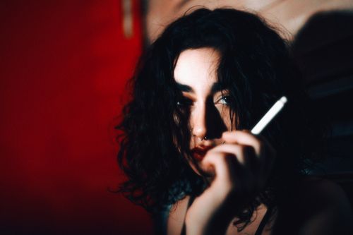 Free Moody portrait of a young woman with dark curly hair, smoking indoors. Stock Photo
