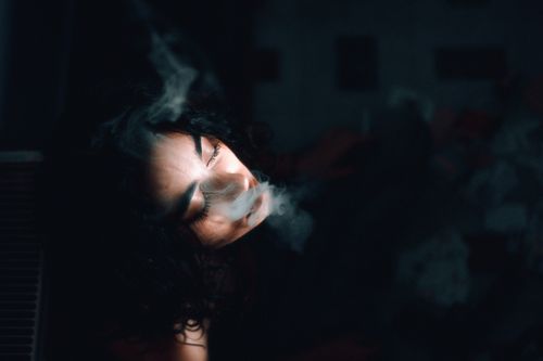 Free Artistic portrait of a woman exhaling smoke in a dark studio setting. Stock Photo