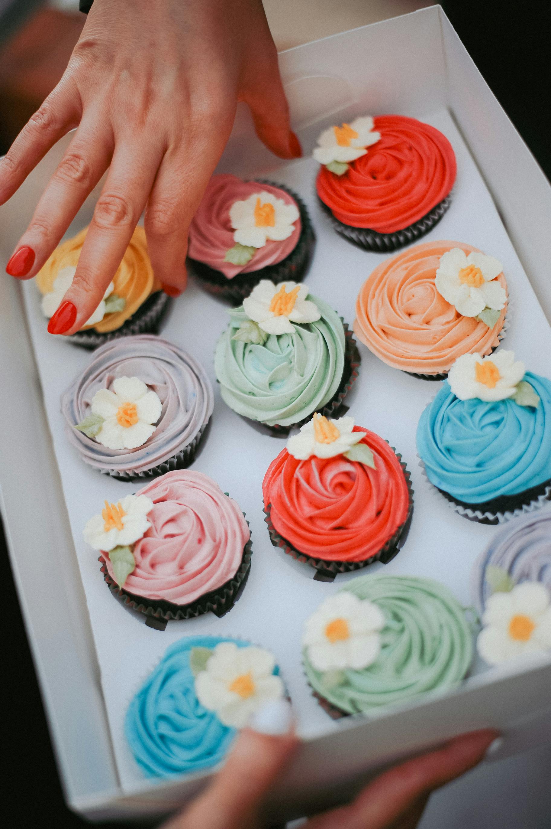 Box of colorful frosted cupcakes with floral icing designs, perfect for celebrations.