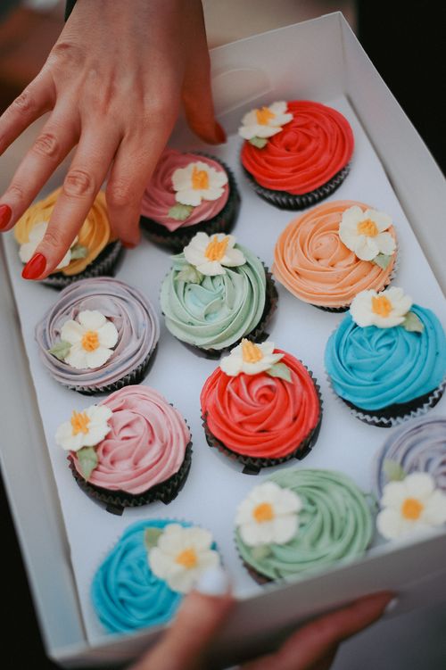 Free A box of vibrant cupcakes, each with floral decorations, presented with a hand reaching in. Stock Photo