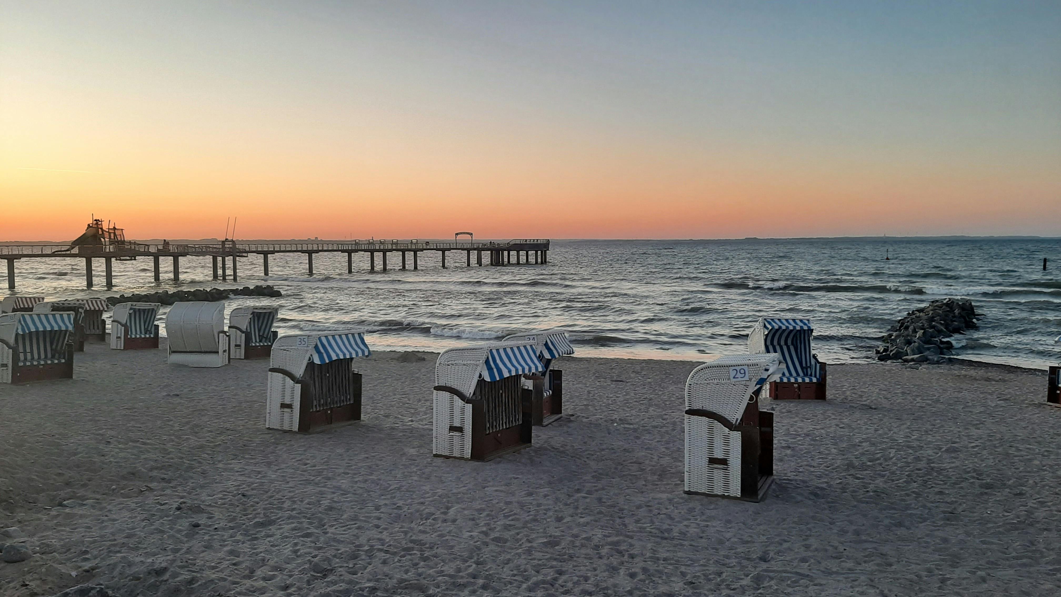Calm sunset view at a beach with empty hooded chairs and pier. Scenic and peaceful.