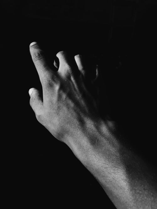 Free Black and white artistic photograph of a human hand reaching up with dramatic shadows. Stock Photo
