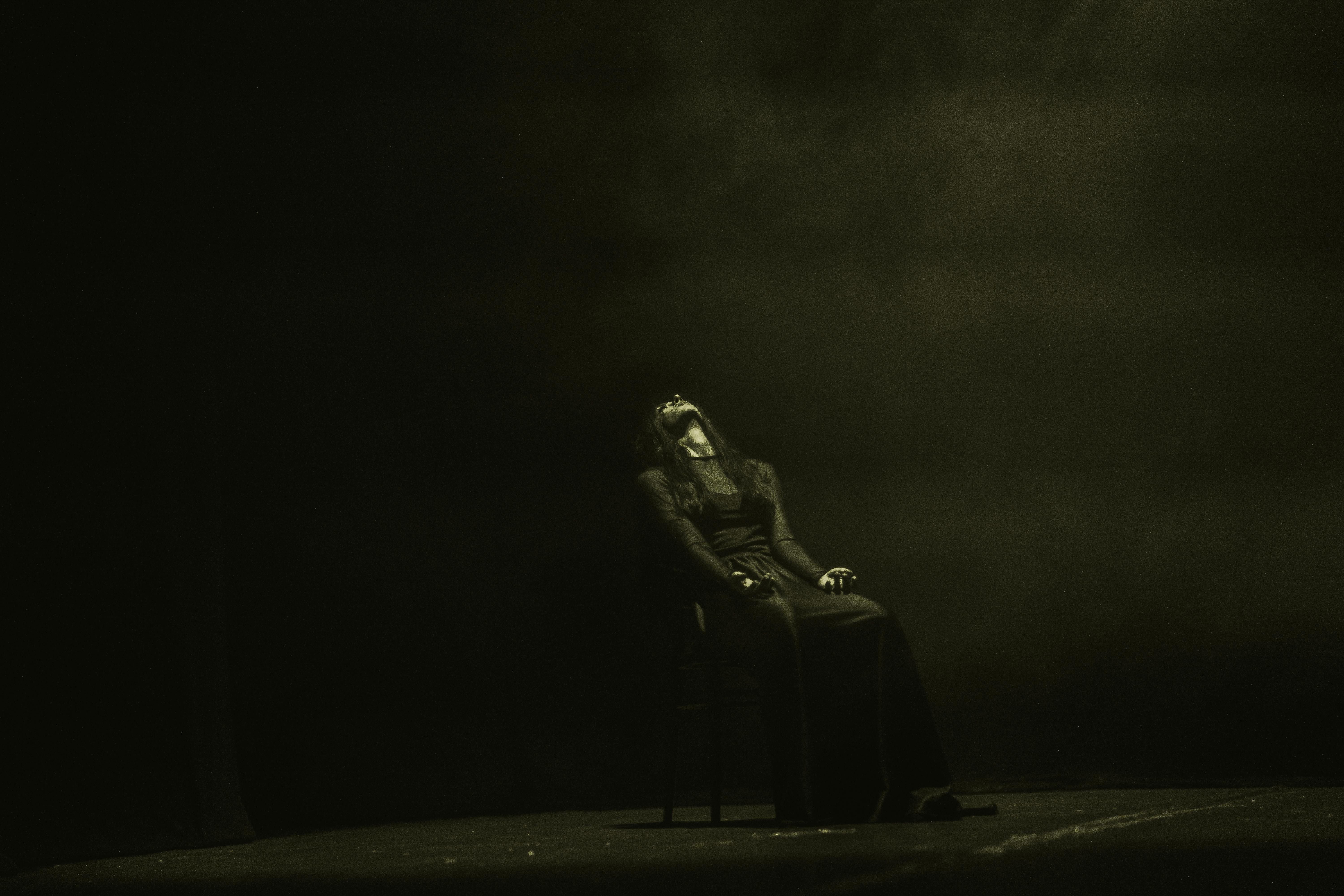 Free Moody stage performance with dramatic lighting and shadows, capturing a solo female artist in contemporary dance. Stock Photo