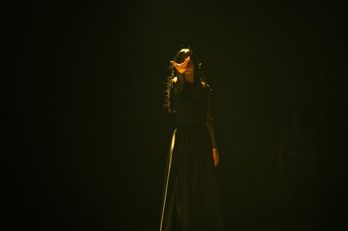 Free Artistic fashion portrait of a woman in a dark dress reaching out, captured in moody studio lighting. Stock Photo