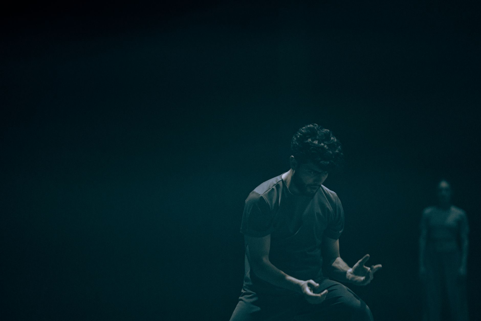 A male dancer performs an emotional piece in a dark studio setting with moody lighting.
