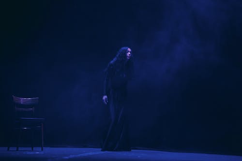 A woman in black standing on stage in front of a chair