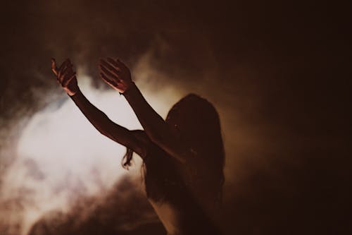 A woman in a dark room with her hands up
