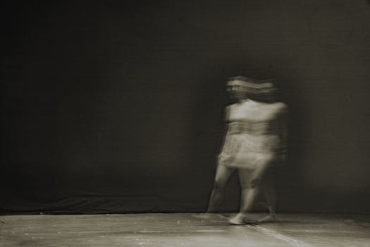 Artistic blurred motion photograph of a person walking on stage, creating a ghostly effect.