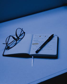 桌上摊开一本笔记本，旁边放着一支笔和一副眼镜，捕捉了学习或规划的本质