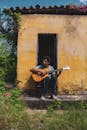 在一个阳光明媚的日子，巴西一栋乡村黄屋外，一名男子弹着吉他