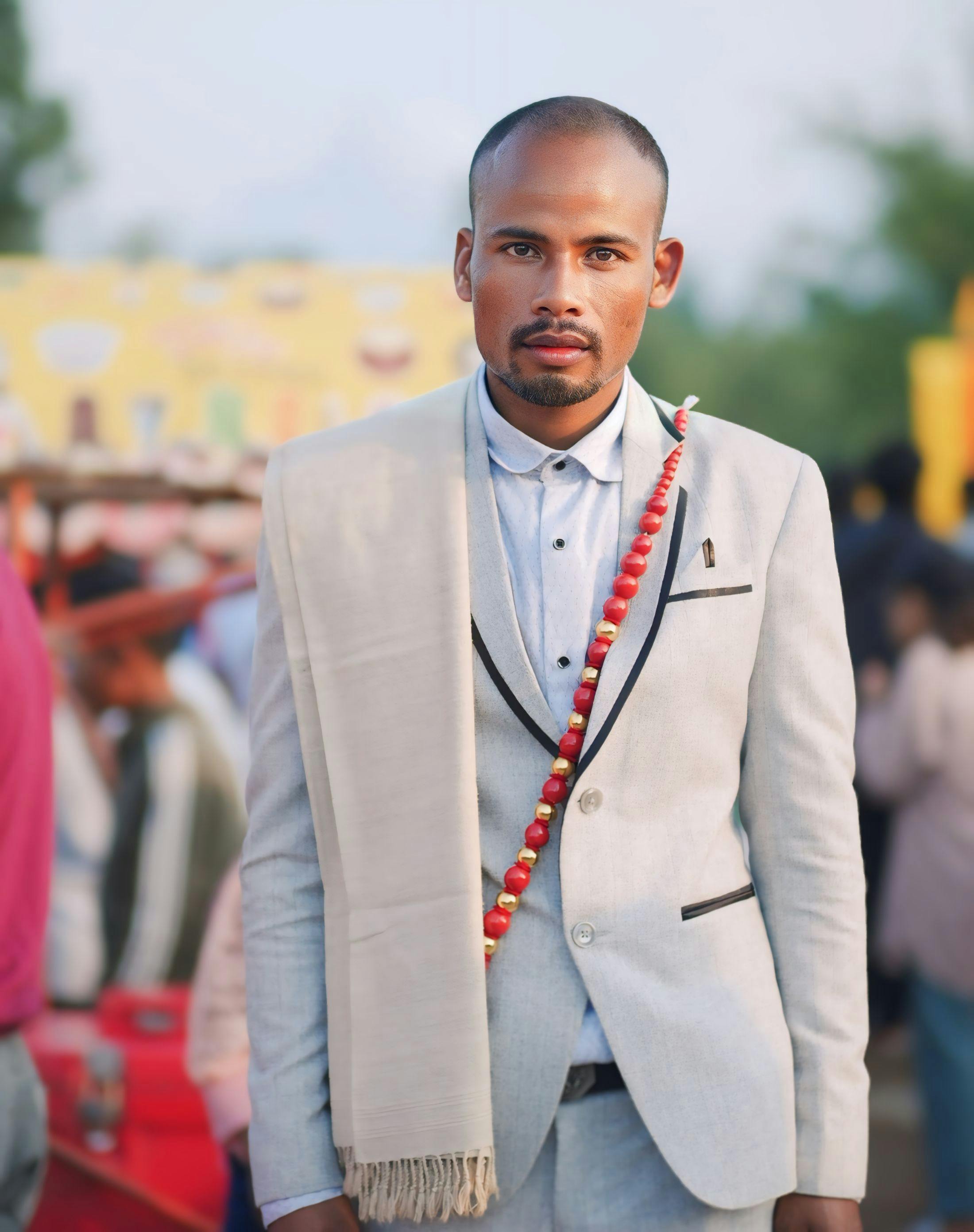 Portrait of an elegantly dressed man in a light suit with a festive garland, standing outdoors.