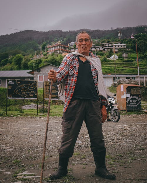 A man standing in front of a village with a stick