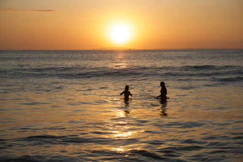 Free Two people wade in the ocean at sunset, creating a peaceful and reflective scene. Stock Photo