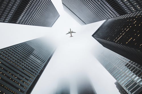 Низкоугловая фотография самолета, пролетающего над высотными зданиями