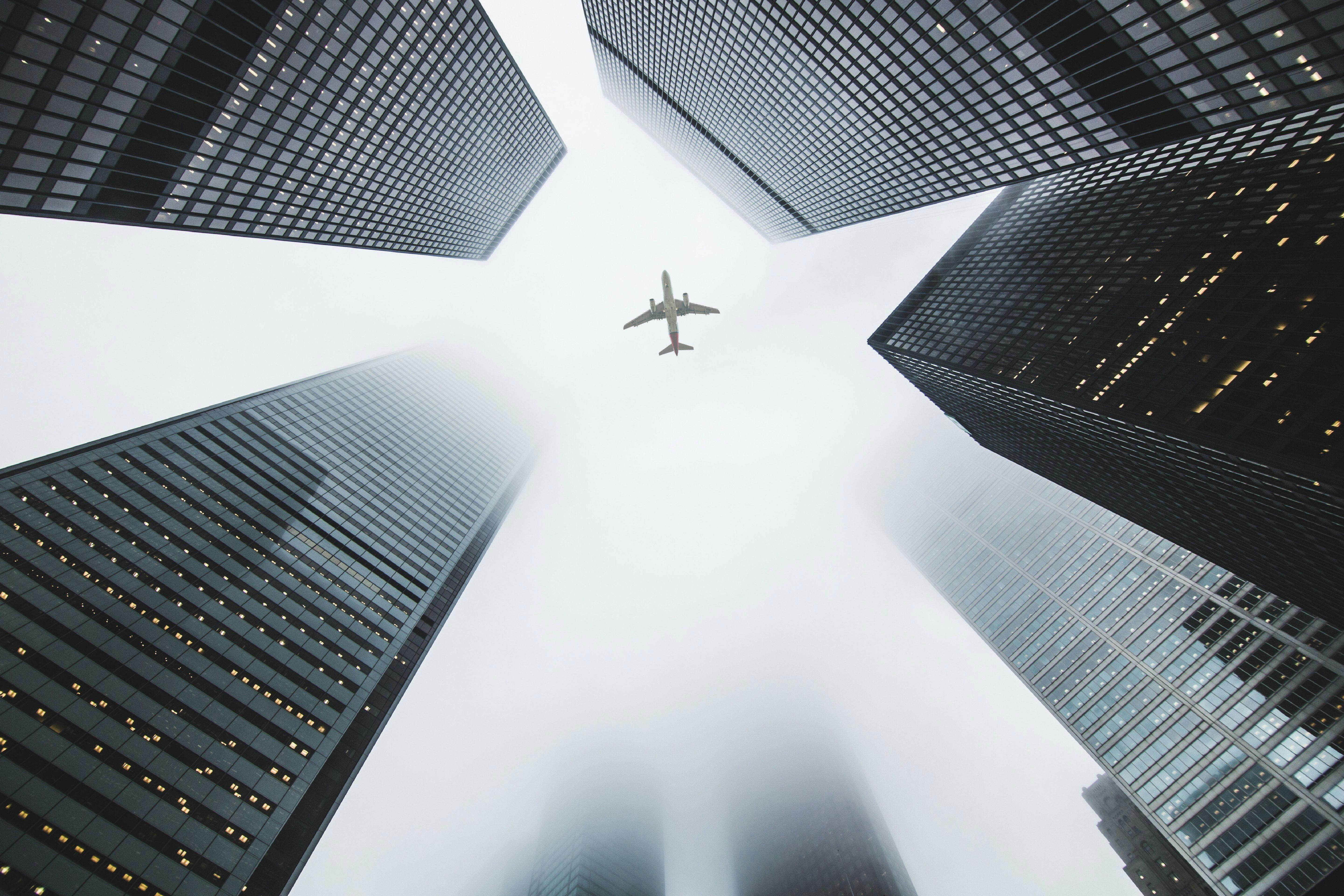 Low Angle Photo of Airplane Flying Over Highrise Buildings · Free