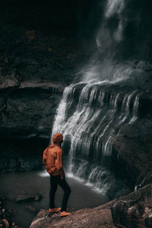 男人站在瀑布上的棕色岩層附近