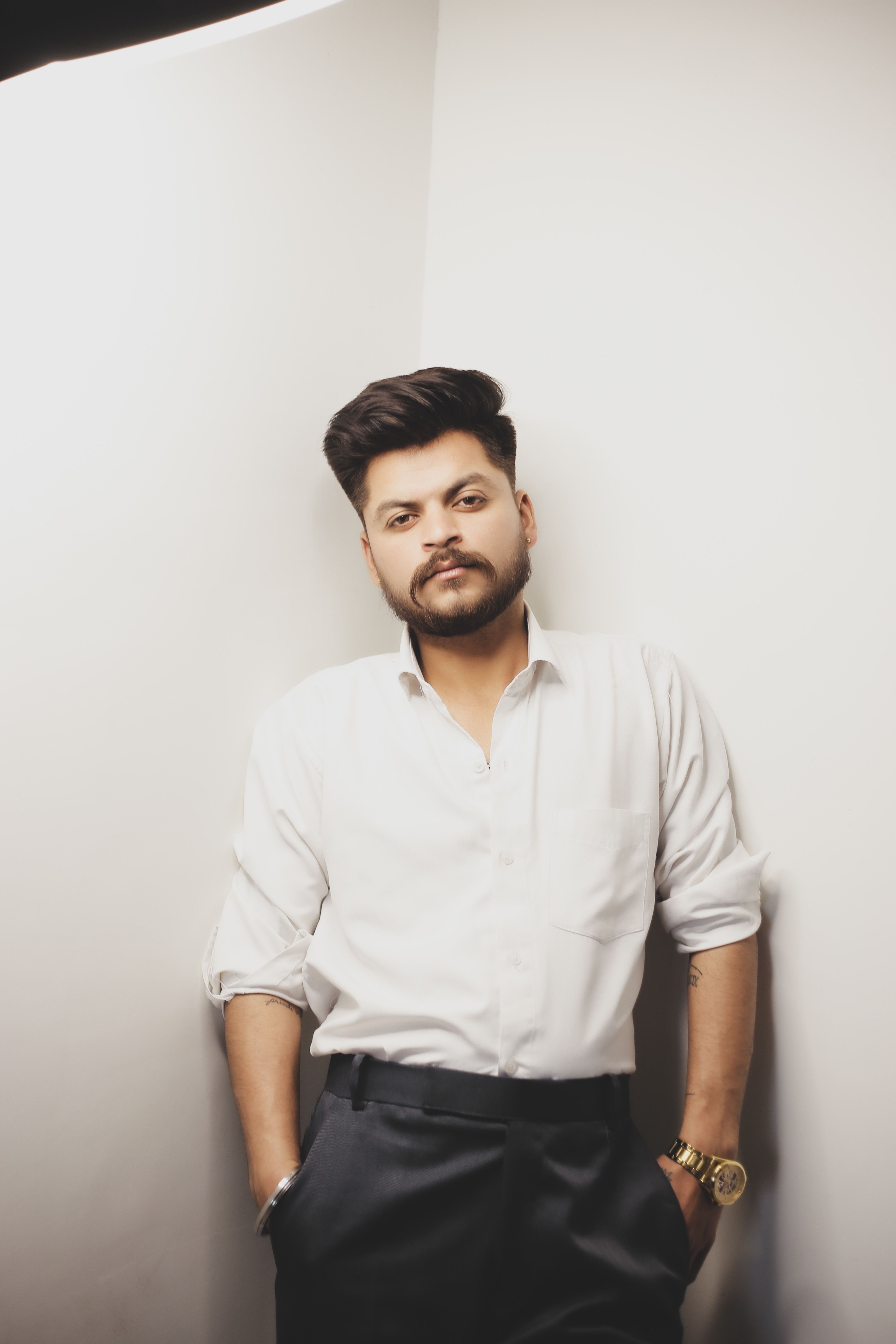 Portrait of a stylish man in a white shirt posing confidently in a studio.