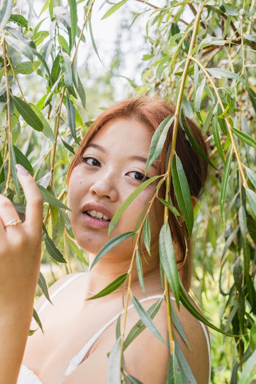 A woman is looking at the camera while holding a willow tree