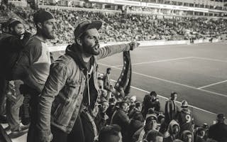Monochrome Photo of Man Wearing Jacket Pointing Finger at Stadium