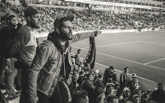 Monochrome Photo of Man Wearing Jacket Pointing Finger at Stadium