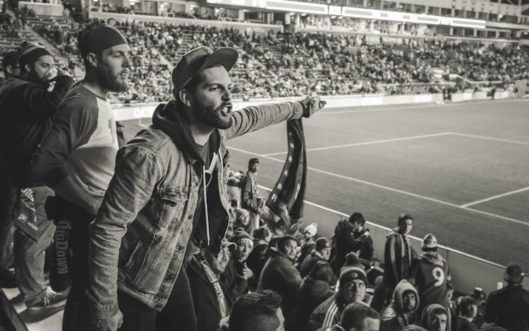 Monochrome Photo Of Man Wearing Jacket Pointing Finger At Stadium