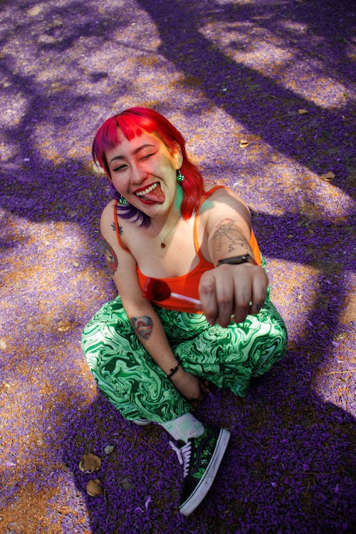 A woman with red hair and tattoos is sitting on the ground