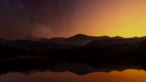 Free Stunning twilight scene with silhouetted hills and a starry sky reflecting in a serene lake. Stock Photo