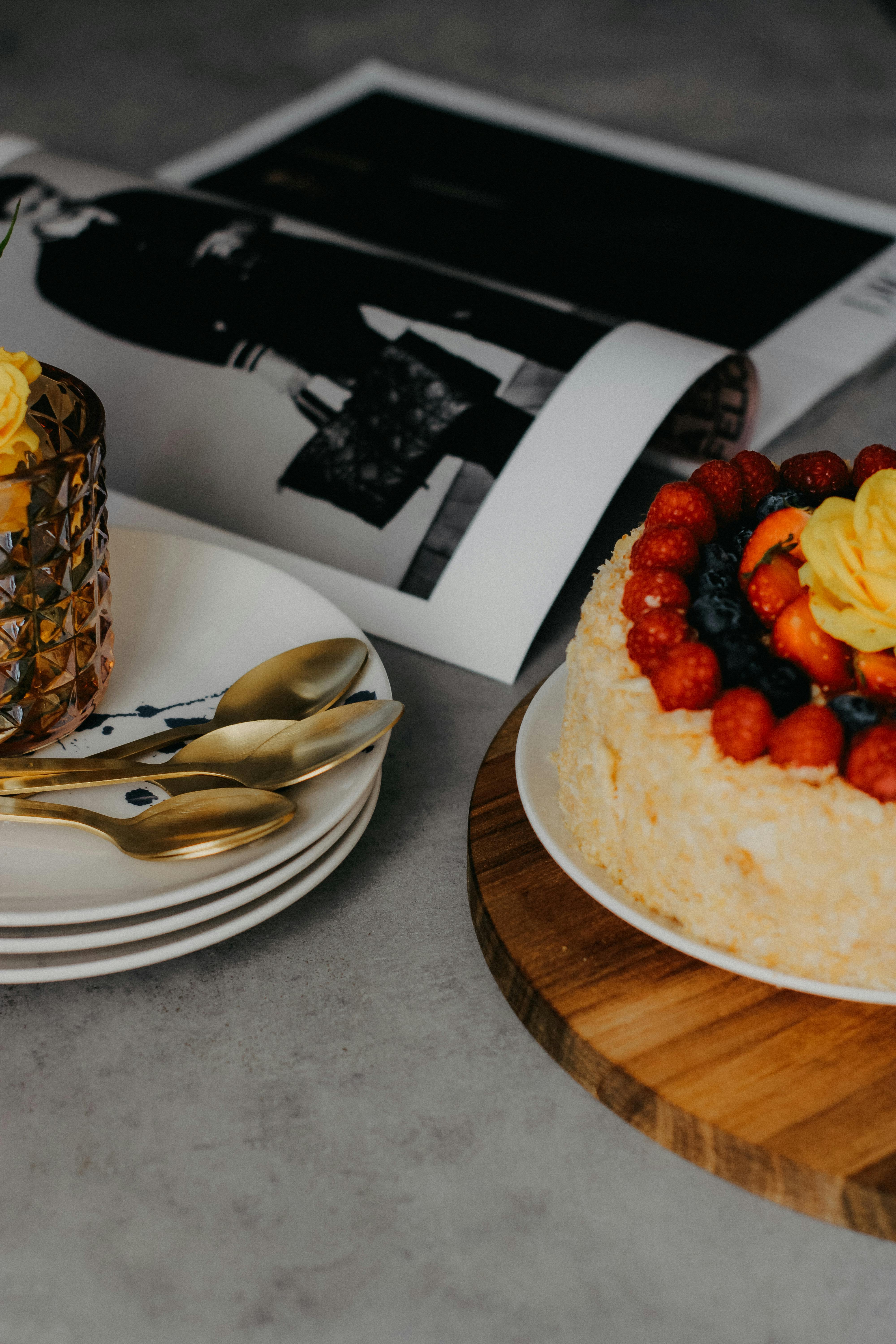 A visually striking fruit-topped cake beside stylish golden cutlery and a fashion magazine.