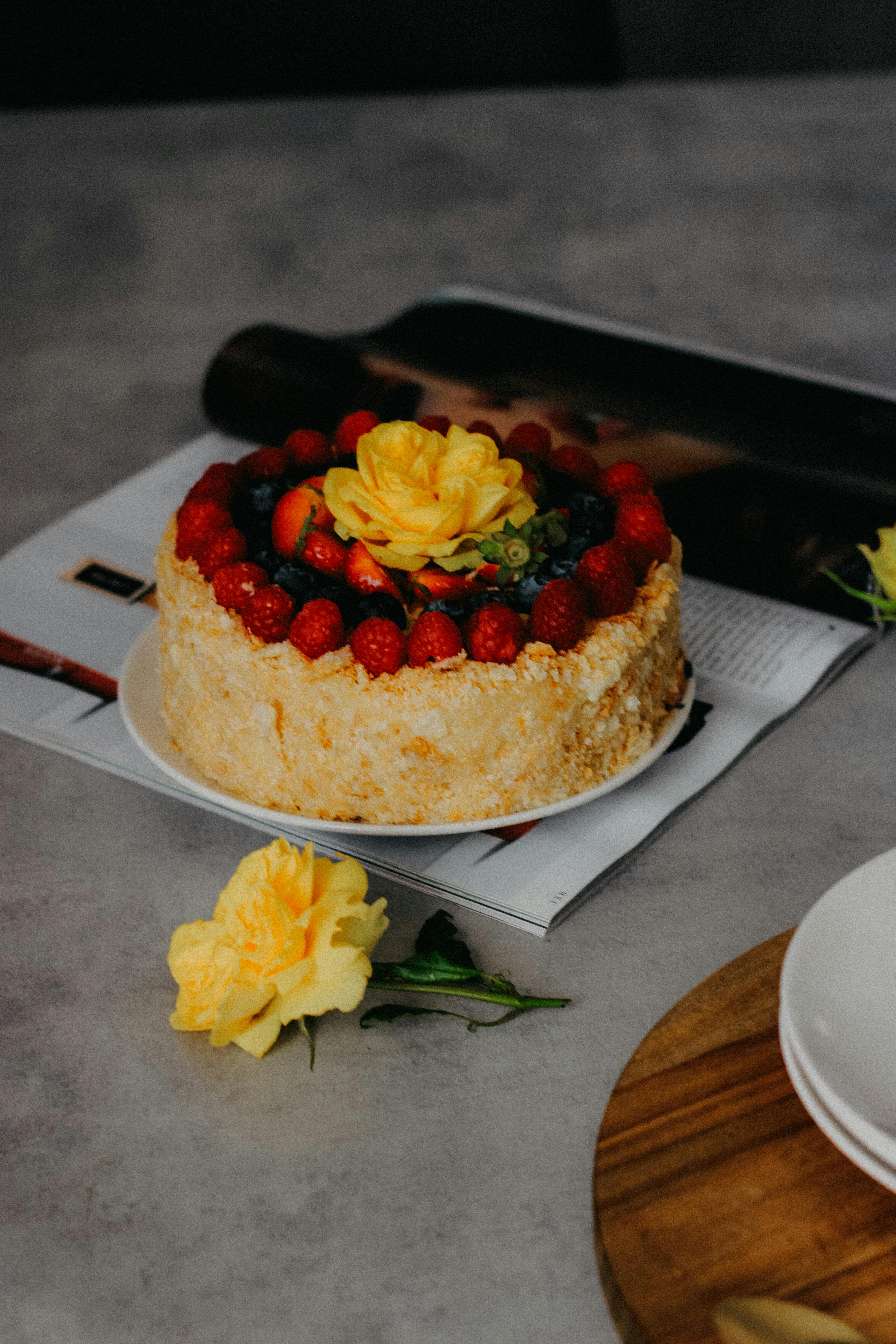 A delectable cake decorated with berries and a yellow rose, perfect for celebrations.