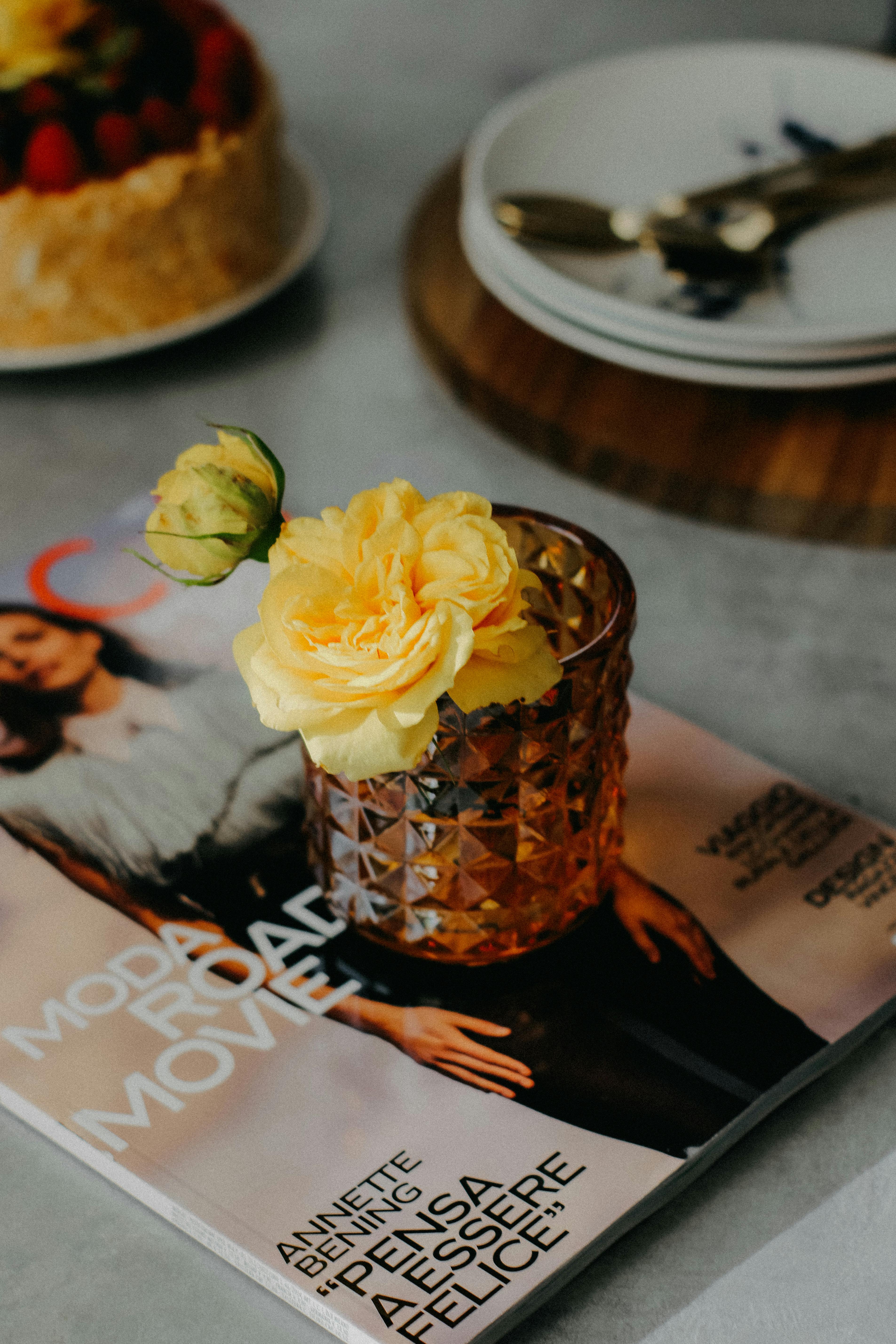 A stylish crystal vase with a yellow rose on a magazine, perfect for home decor inspiration.