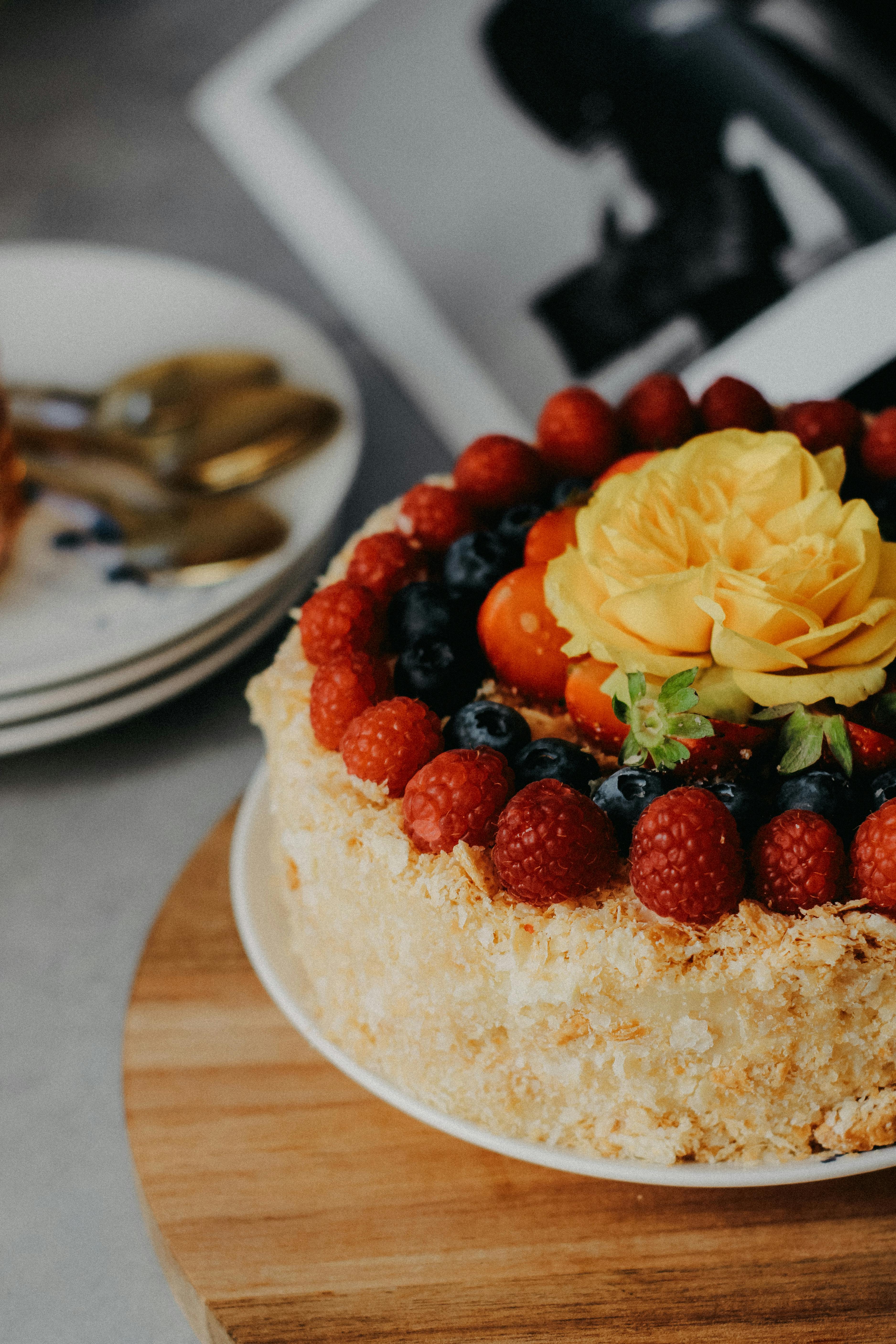 Delicious cake adorned with berries and a yellow rose, perfect for celebrations.