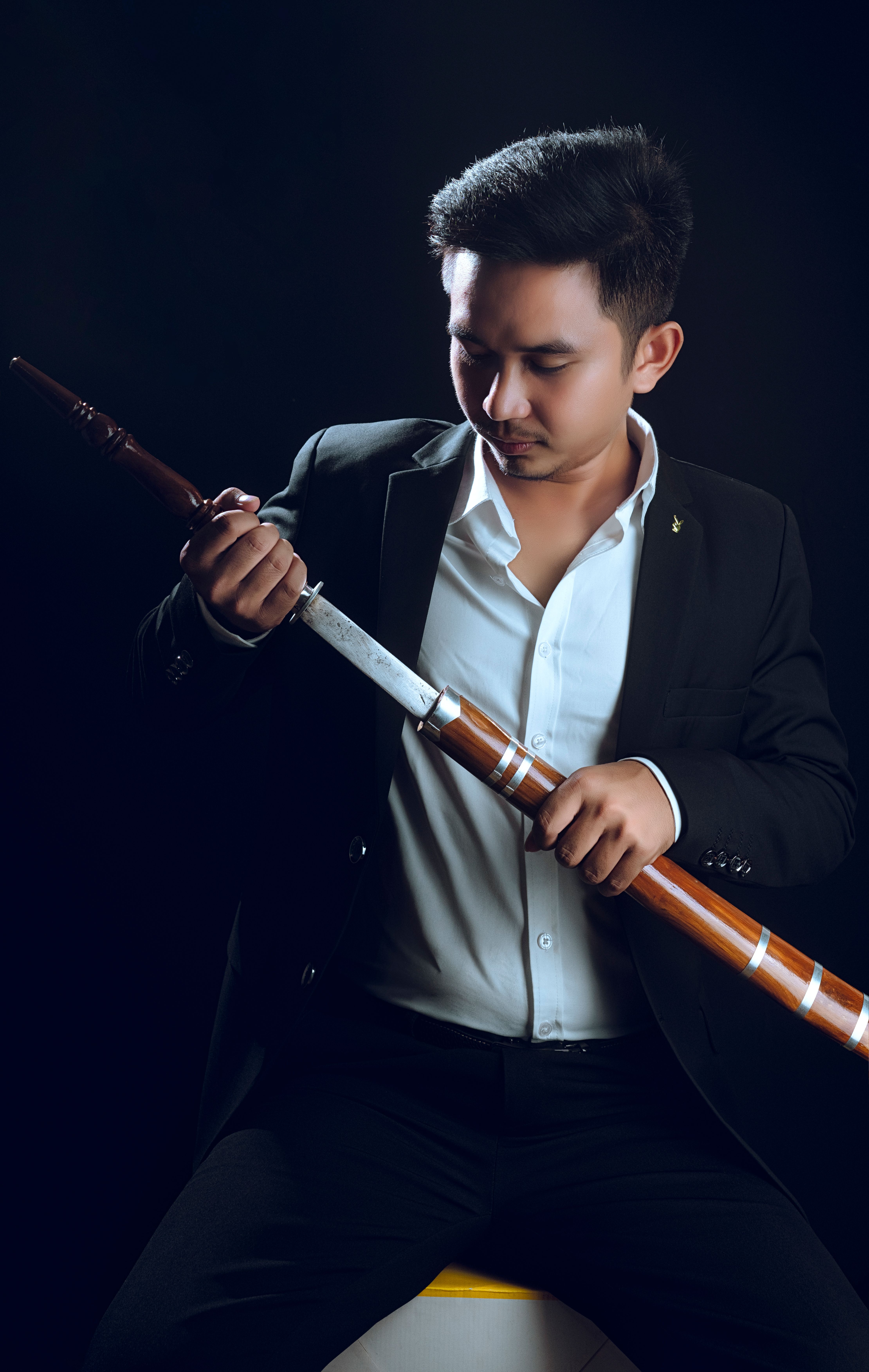 Portrait of a fashionable man in a black suit holding a katana, posing in a studio shoot.