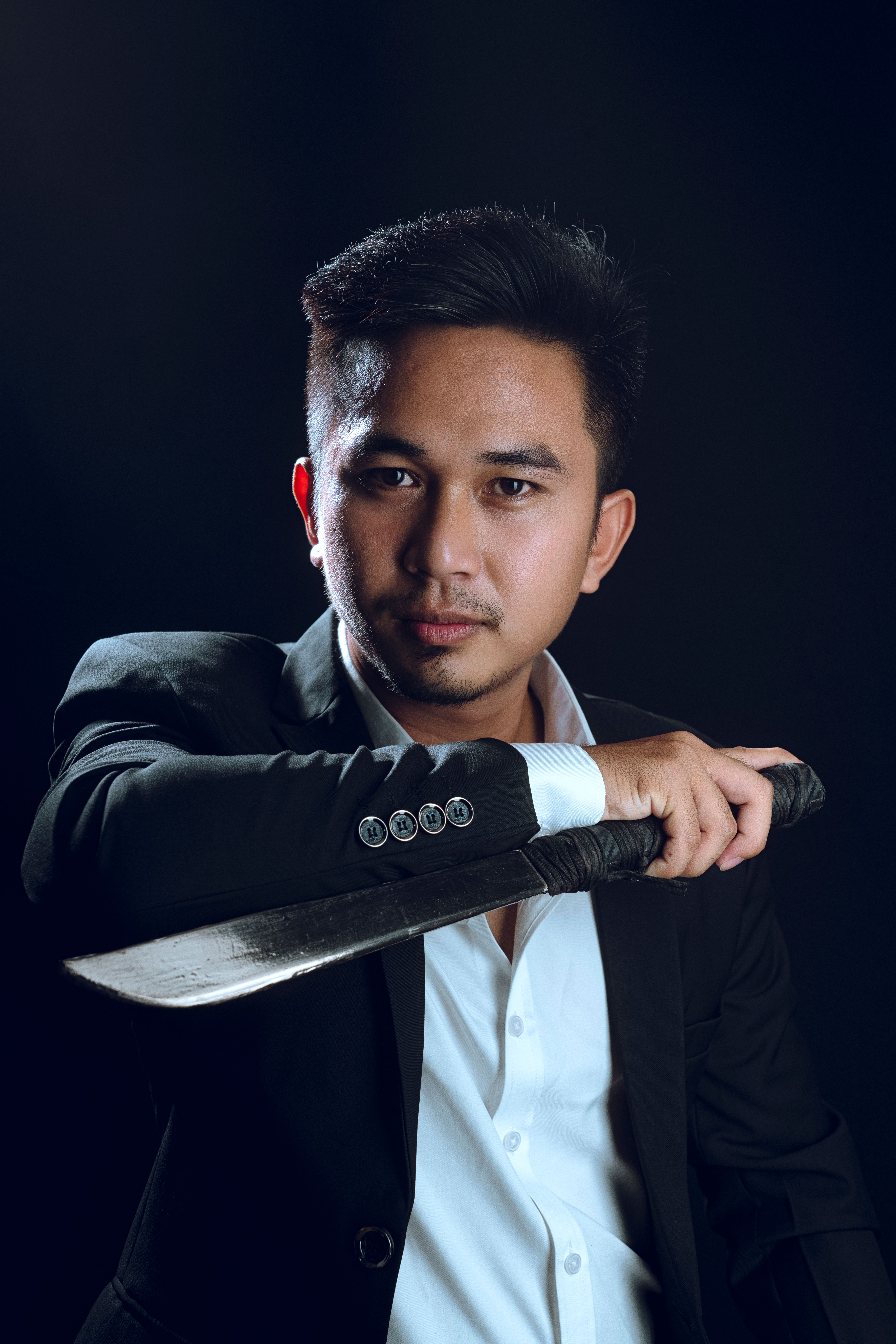 Portrait of a confident man in a suit holding a knife against a black background.