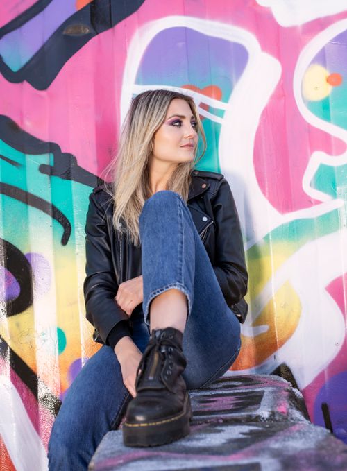 Free A fashionable woman sitting by a vibrant graffiti wall, showcasing urban style. Stock Photo
