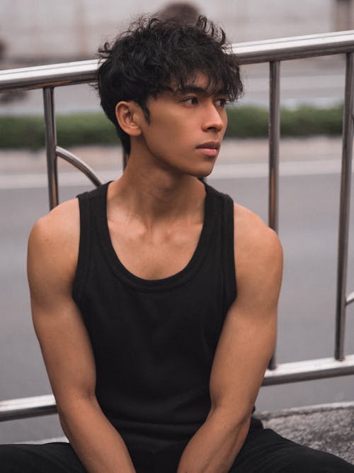 A young man in black tank top sitting on a bench