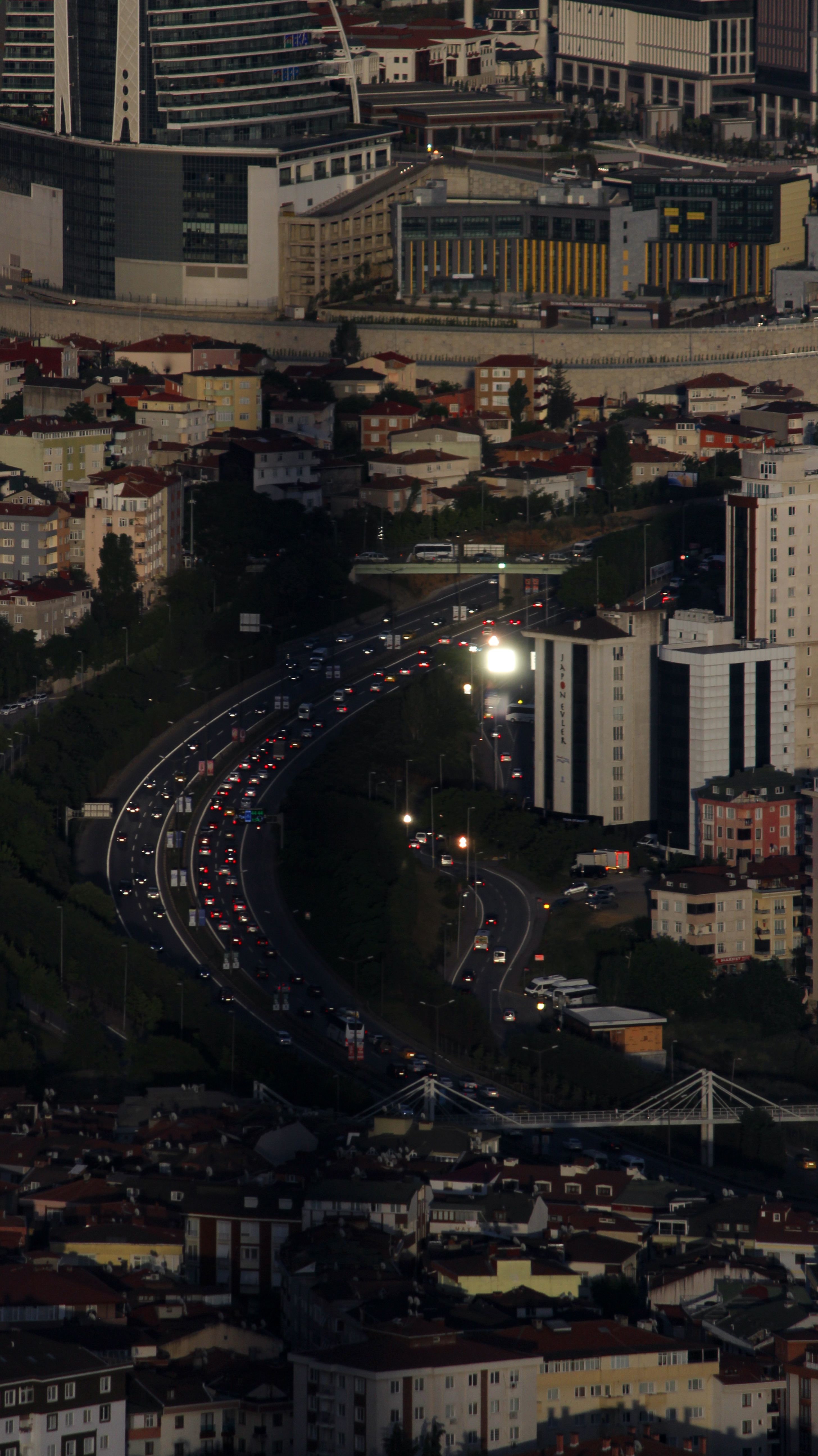Aerial shot showcasing the bustling cityscape with winding roads and high-rise buildings at dusk.