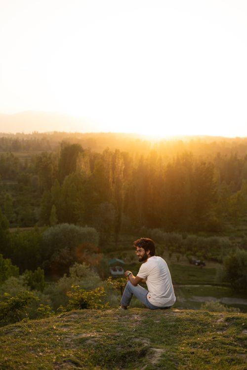 Free A man sitting on a hilltop enjoying the scenic sunset view of Srinagar's lush landscape. Stock Photo