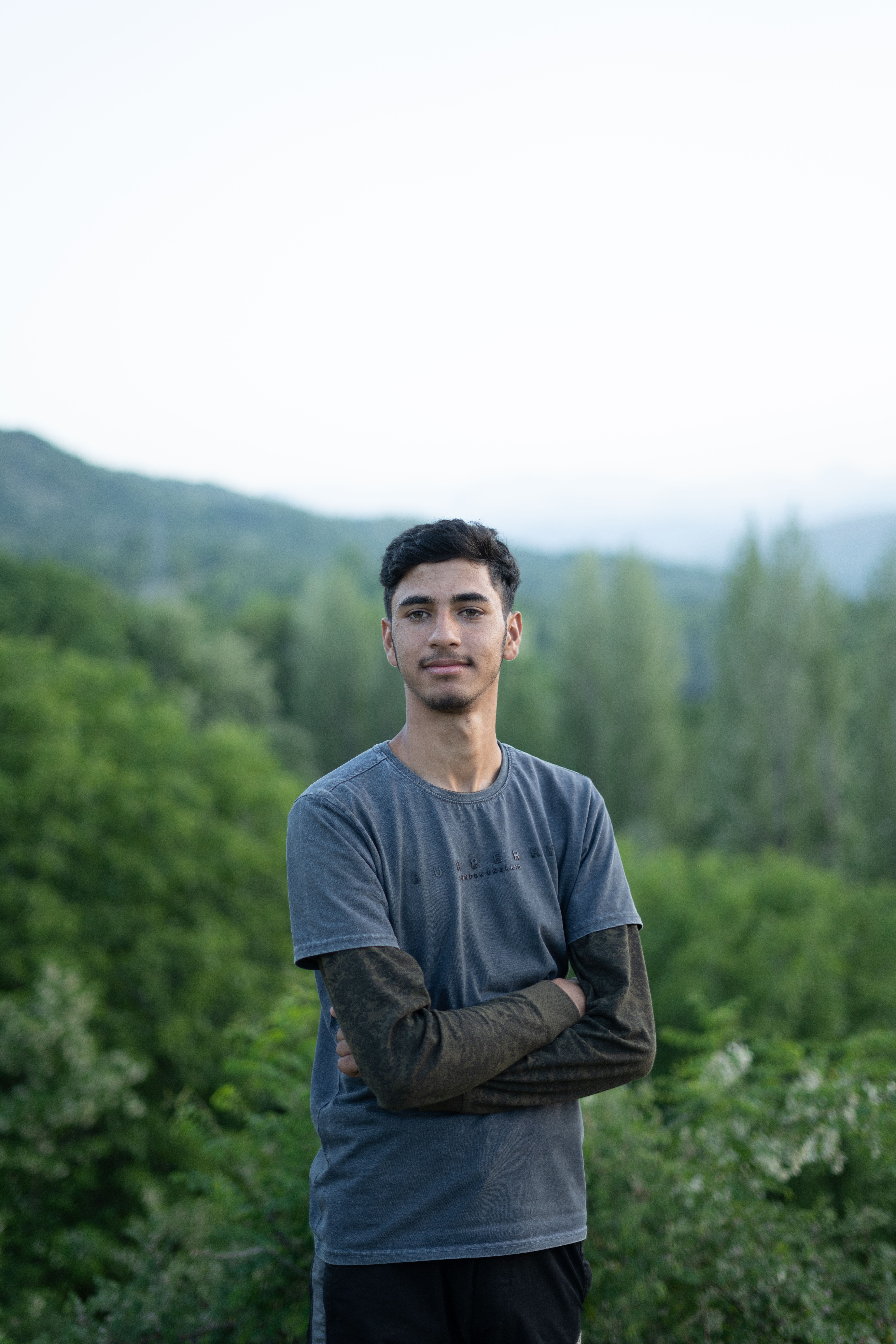 Portrait of a young man standing with crossed arms in a lush Srinagar landscape, conveying tranquility.