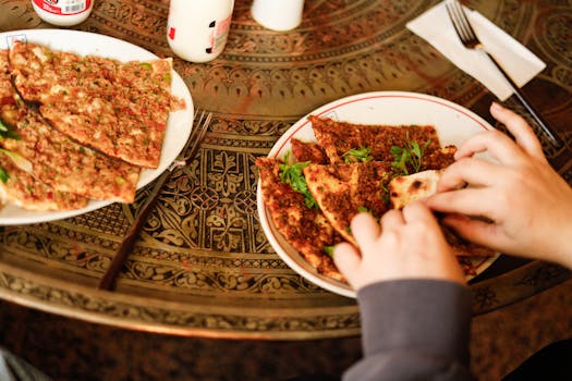 Hands serving traditional Turkish lahmacun on an ornate table, showcasing authentic cuisine.