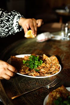Close-up of hands squeezing lemon over traditional Turkish lahmacun at a table.