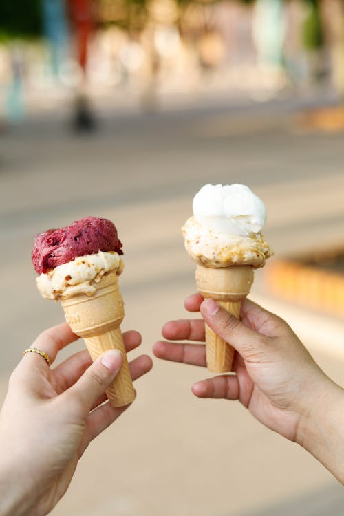 Two hands holding ice cream cones with different flavors