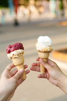 Two hands holding ice cream cones with double scoops on a sunny day.