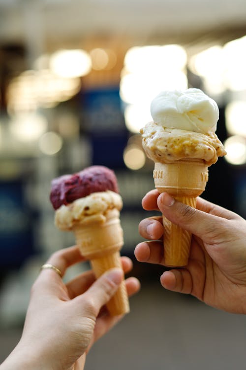 Two hands holding ice cream cones with different flavors