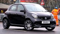 一辆光滑的黑色汽车在城市街道上被道路施工工人包围