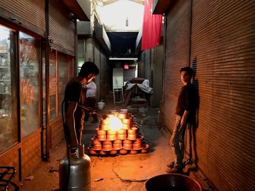 Two men are standing in a narrow alley with pots of fire