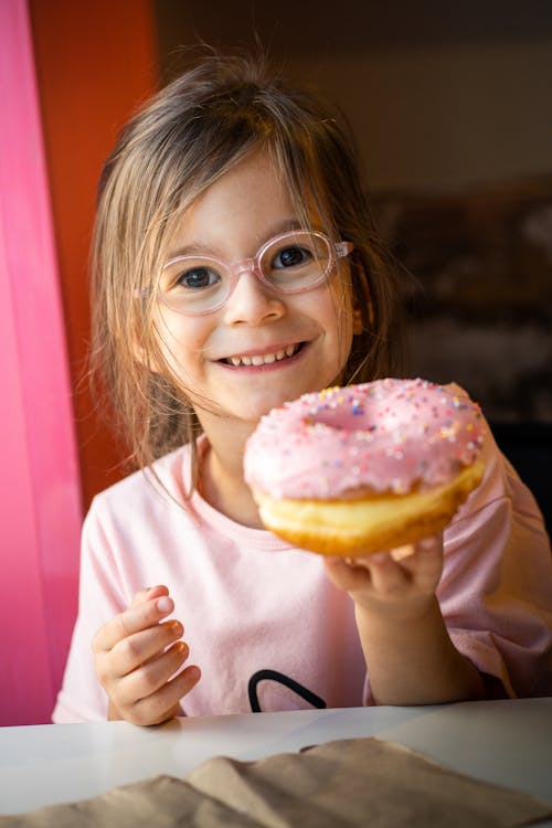 A little girl with glasses holding a donut